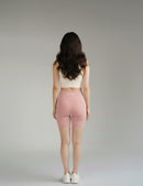 Back pose of a woman wearing a BELVYNN premium beige sports bra and pink shorts on a gray background