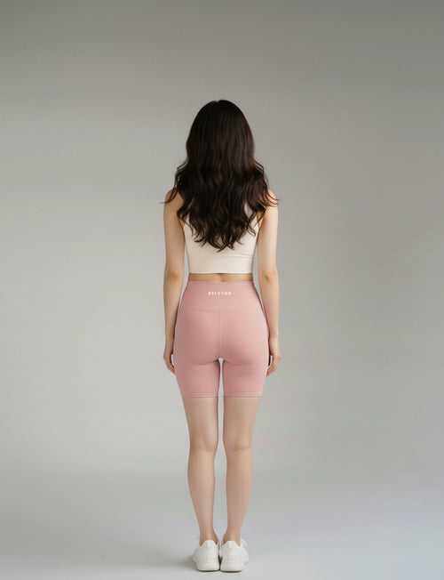 Back pose of a woman wearing a BELVYNN premium beige sports bra and pink shorts on a gray background