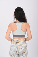 Back pose view of a Woman wearing a BELVYNN Signature ash green sports bra and floral leggings on a white background