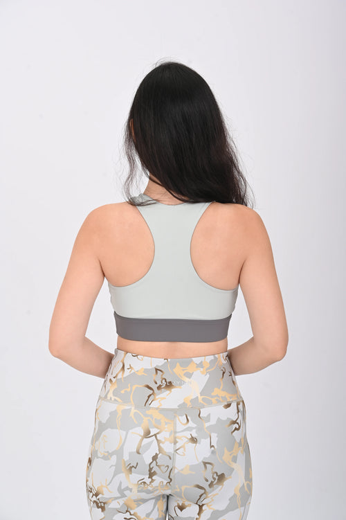 Back pose view of a Woman wearing a BELVYNN Signature ash green sports bra and floral leggings on a white background