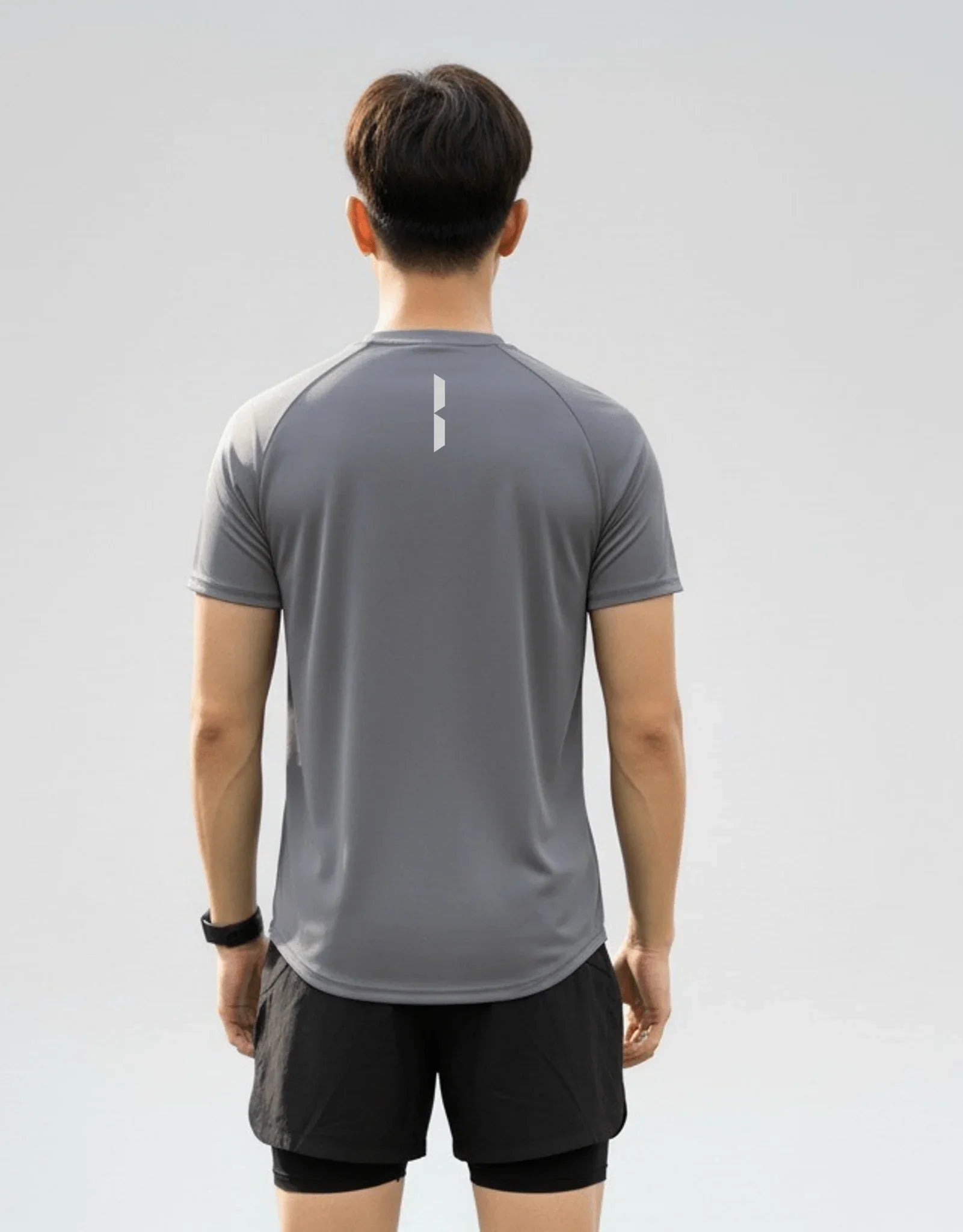 Back view of a male athlete wearing the BELVYNN Men’s Performance T-shirt in gray, highlighting the V-taper silhouette and climate-tech moisture management.