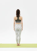 Back view pose of a woman wearing a BELVYNN signature green sports bra and patterned leggings on a white background