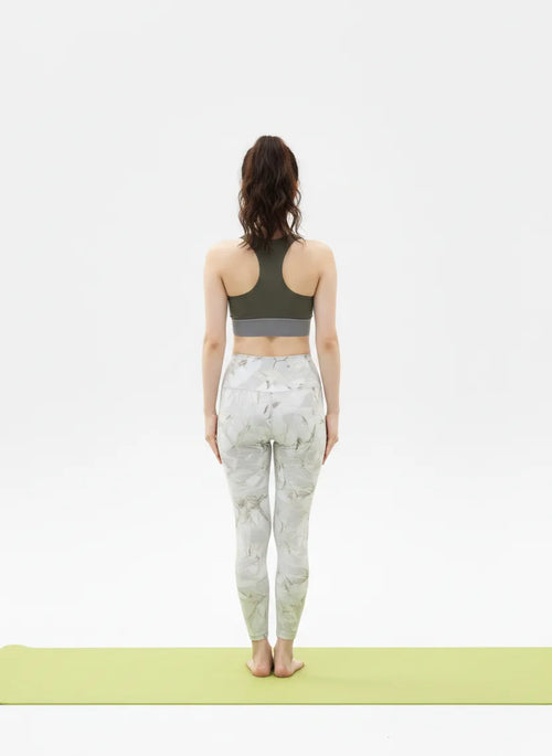 Back view pose of a woman wearing a BELVYNN signature green sports bra and patterned leggings on a white background