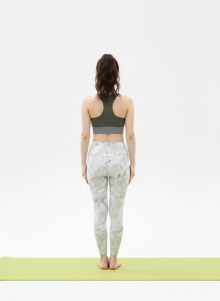 Back view pose of a woman wearing a BELVYNN signature green sports bra and patterned leggings on a white background