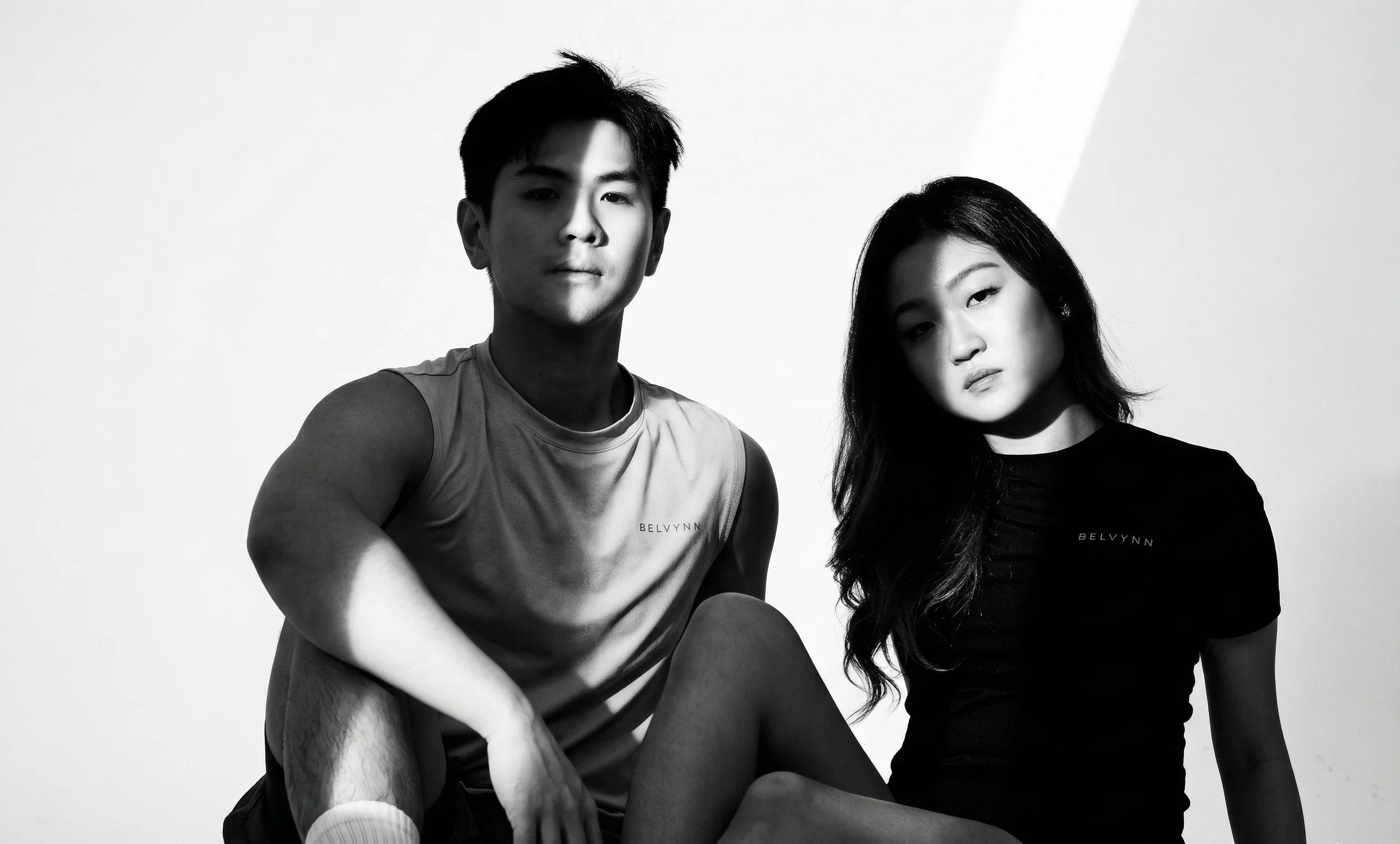 Black and white photo of two people sitting on a white background wearing BELVYNN Premium activewear clothes