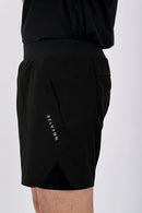 Close up side view of a person standing wearing BELVYNN premium black shorts and black tank top against a white background