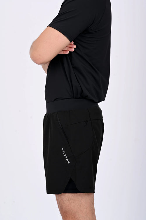 Close up side view of a person wearing BELVYNN premium black shorts and black tank top against a white background