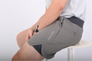 Close up view of a person sitting on a white stool wearing BELVYNN premium gray shorts and gray tank top against a white background