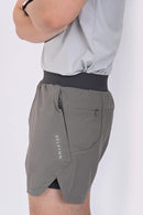 Close up view of a person standing wearing BELVYNN premium gray shorts and gray tank top against a white background