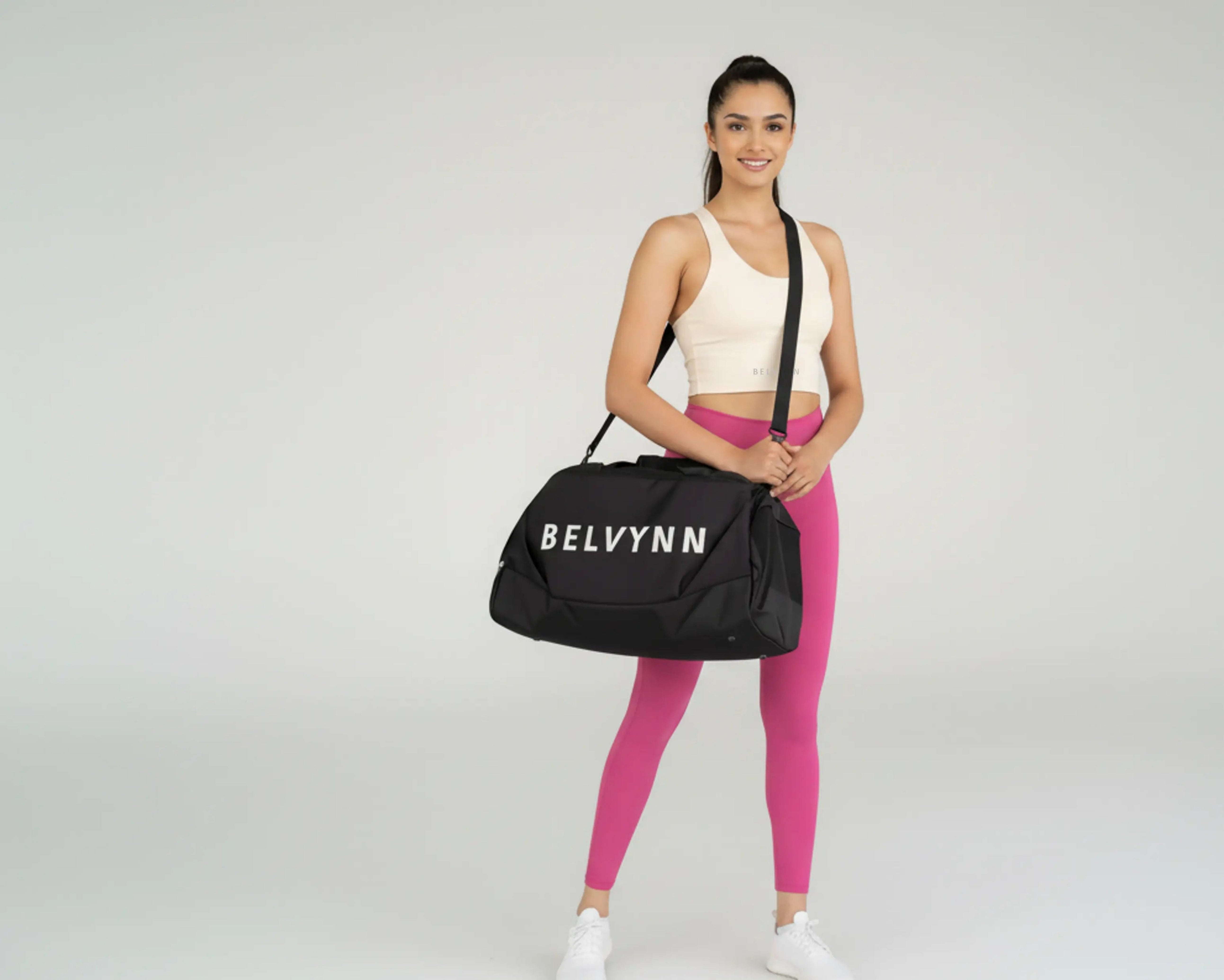 Woman holding a black duffel bag with 'BELVYNN' branding on a gray background