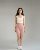 Front view of a woman wearing a BELVYNN premium beige sports bra and pink shorts on a gray background