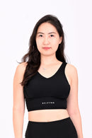 Front view of a woman wearing a black sports bra and black yoga pants a white background