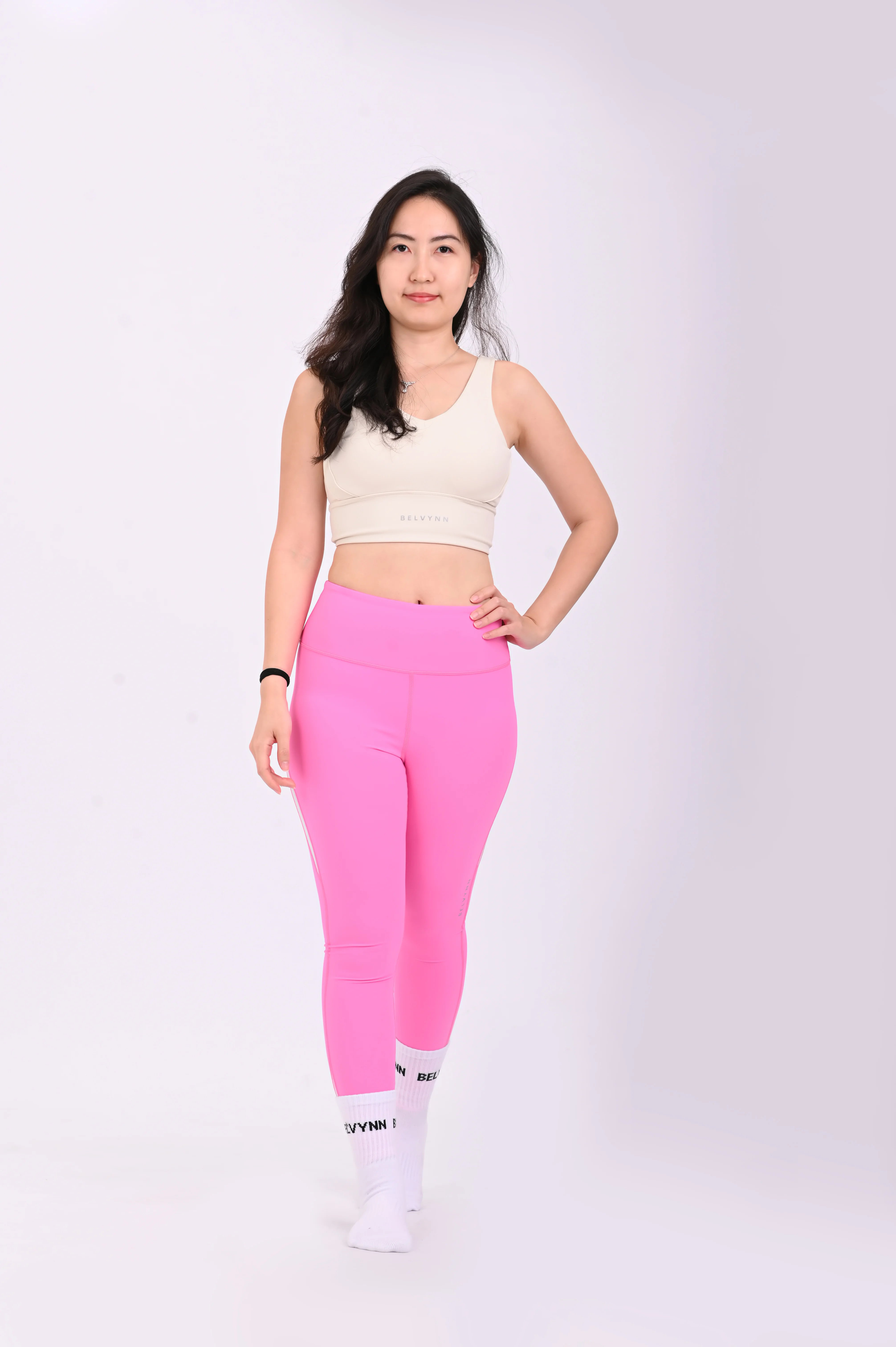 Front view walking pose of a woman wearing BELVYNN Premium beige sports bra and pink leggings on a white background