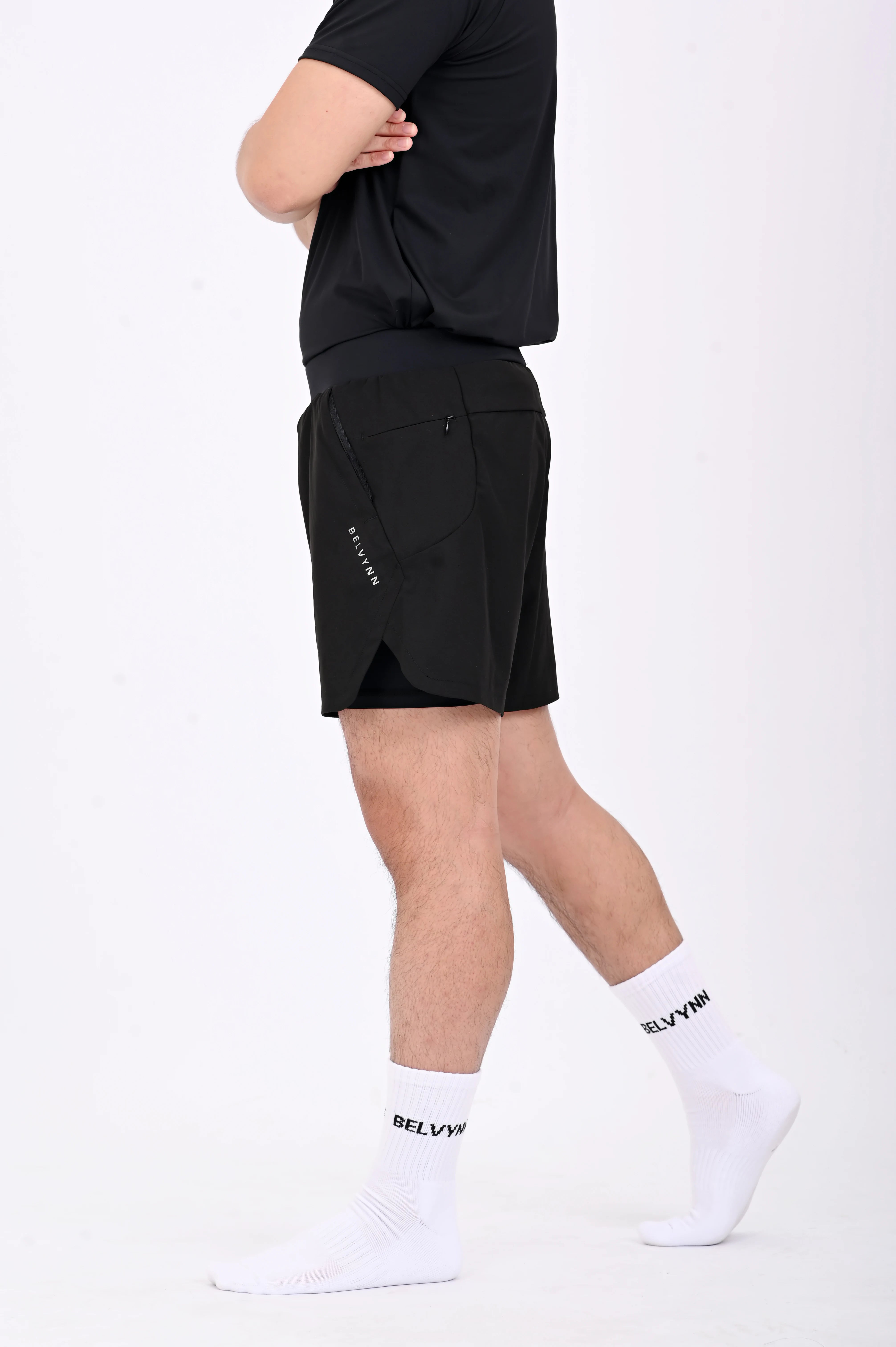 Side view of a person walking wearing BELVYNN premium black shorts and black tank top against a white background