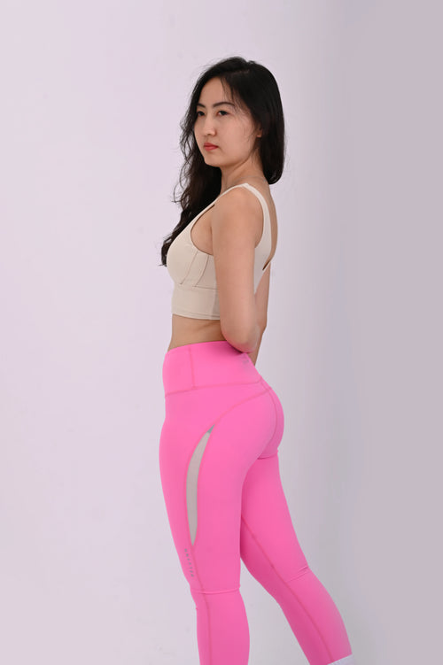 Side view pose of a woman wearing BELVYNN Premium beige sports bra and pink leggings on a white background