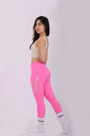 Side view standing pose of a woman wearing BELVYNN Premium beige sports bra and pink leggings on a white background