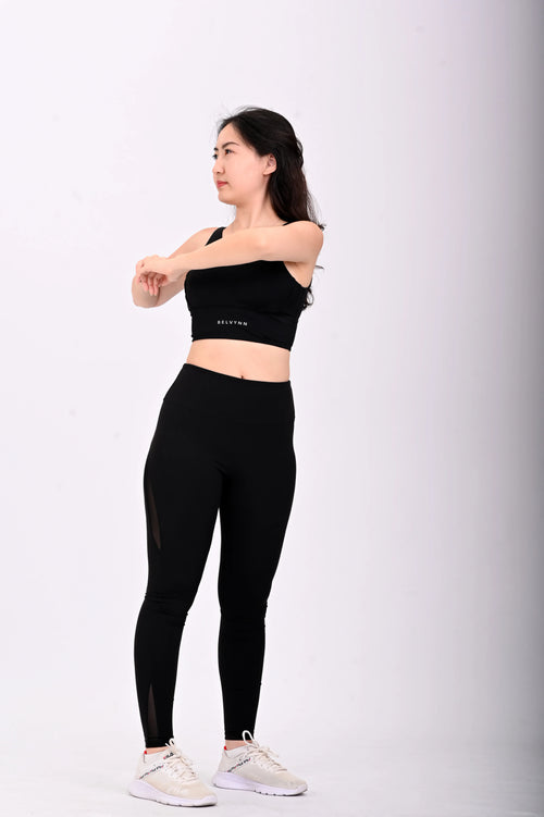 Sideview pose of a Woman wearing a BELVYNN Premium black athletic outfit with visible branding on a white background