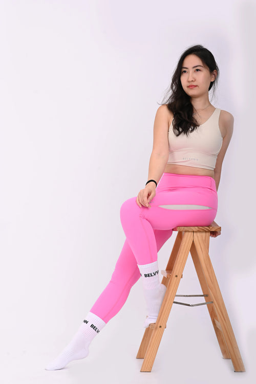 Sitting pose of a woman wearing BELVYNN Premium beige sports bra and pink leggings on a white background