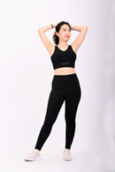 Standing pose of a Woman wearing a BELVYNN black athletic outfit with a visible brand logo on a white background