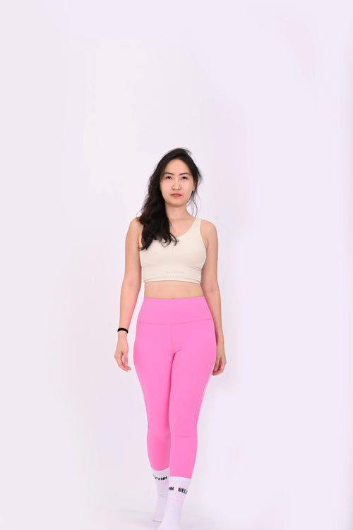 Walking pose of a woman wearing BELVYNN Premium beige sports bra and pink leggings on a white background