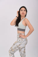 Woman wearing a BELVYNN Signature light green sports bra and patterned leggings on a white background