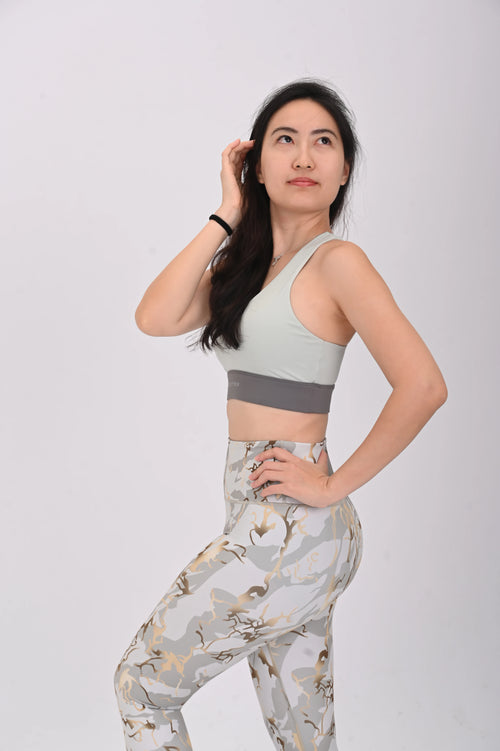 Woman wearing a BELVYNN Signature light green sports bra and patterned leggings on a white background