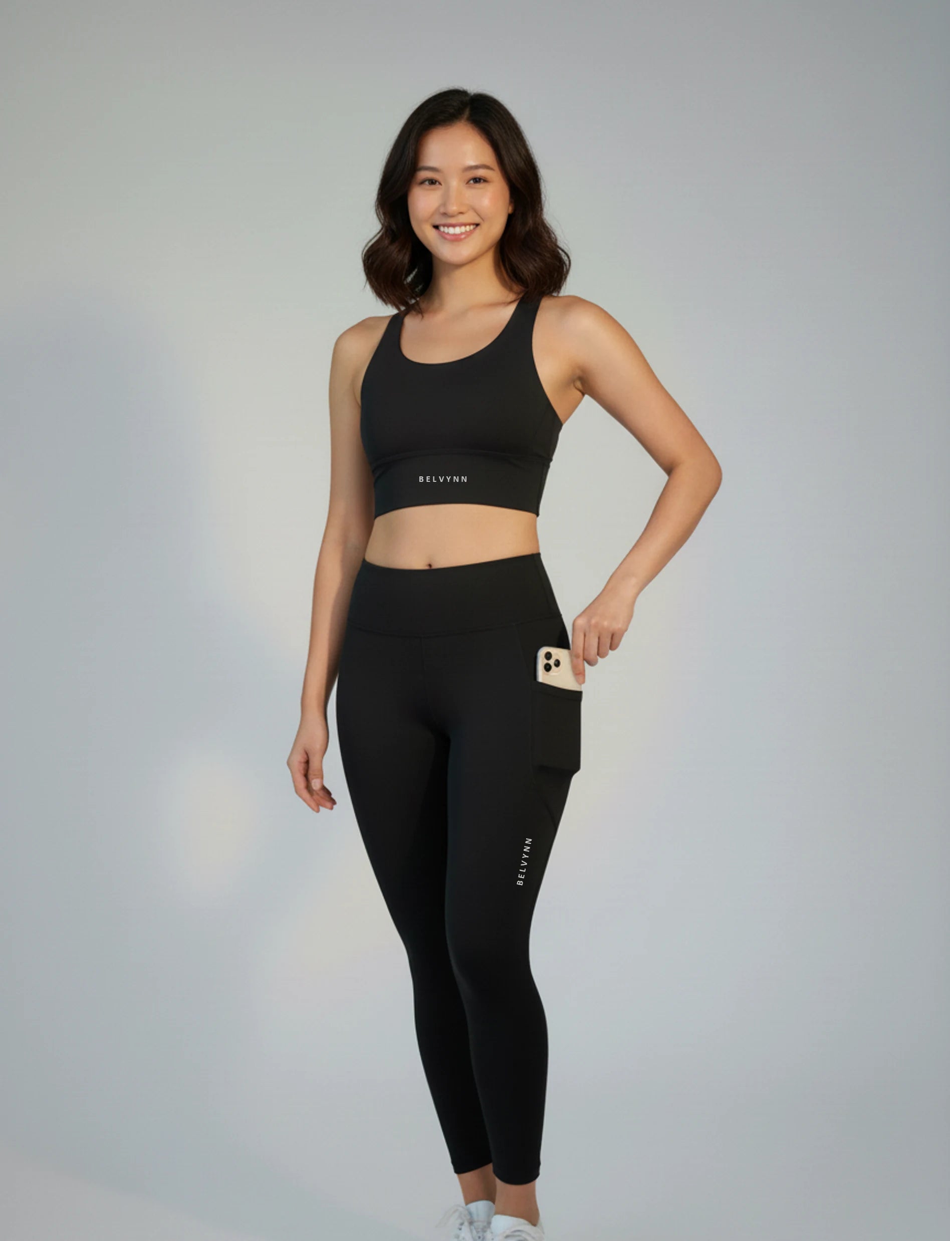 Woman wearing a BELVYNN premium black athletic bra and leggings with visible branding on a gray background
