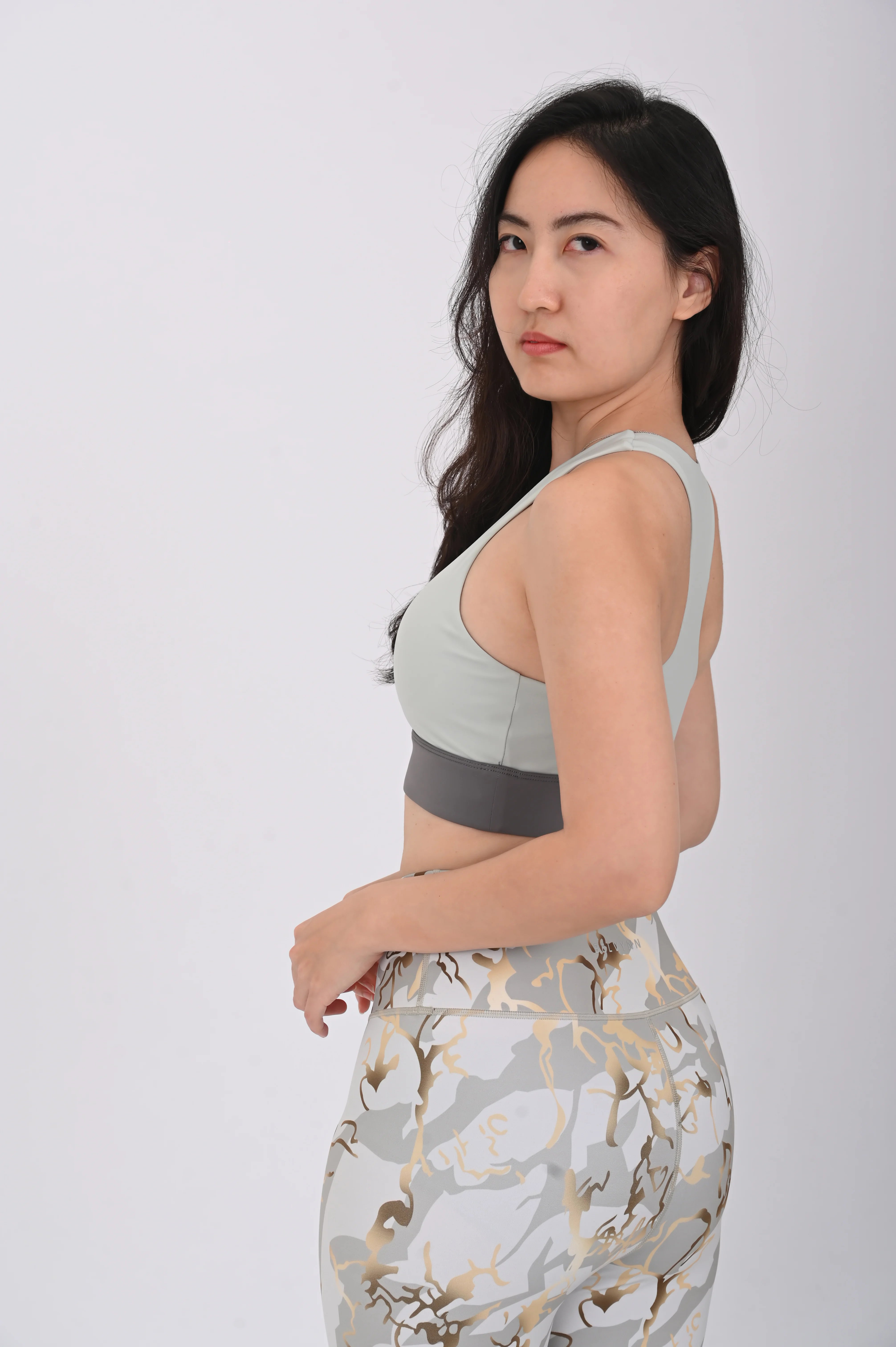 Woman wearing a BELVYNN premium light green sports bra and patterned leggings on a white background